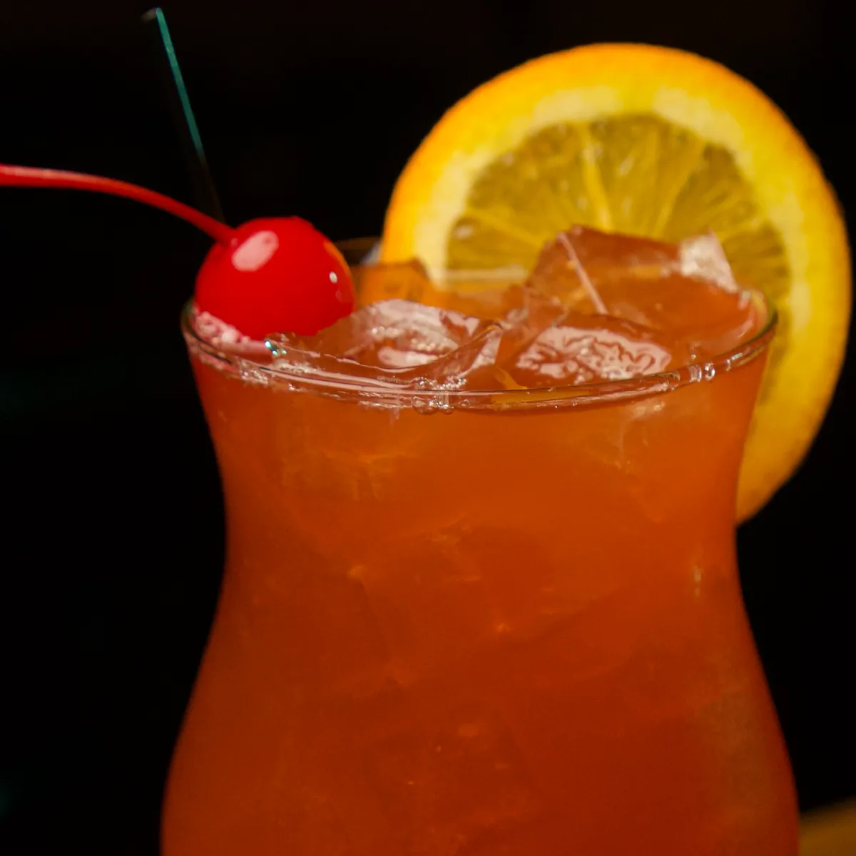 An orange cocktail with a cherry and an orange wheel
