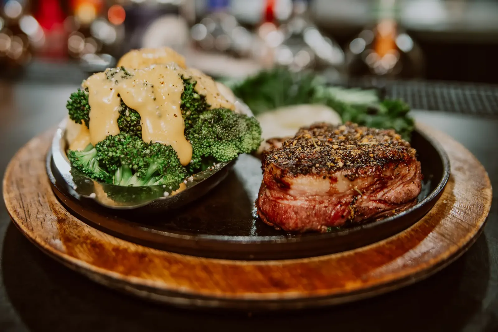 A bacon-wrapped filet on a sizzling skillet with broccoli and cheese sauce